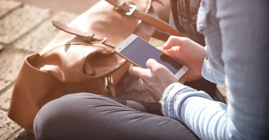 Woman sitting with smartphone and brown bag in sunlight.